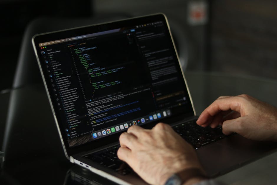 A close-up view of a person's hands typing on a laptop keyboard, with the screen displaying lines of code in a dark-themed editor. The scene suggests a focus on digital work, possibly related to garde